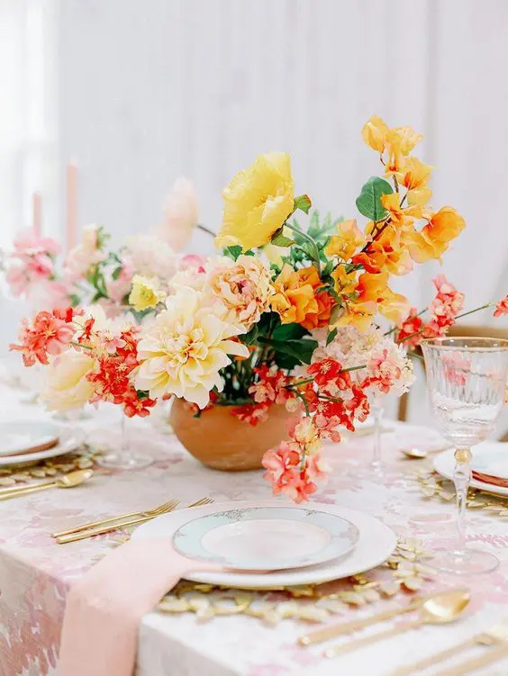 a fabulous colorful wedding centerpiece of yellow poppies and dahlias, pink and orange blooms and greenery looks gorgeous