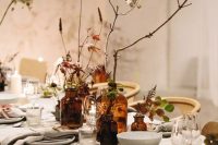 a fall cluster wedding centerpiece of apothecary bottles, blooms and bold foliage, branches and greenery is a cool idea