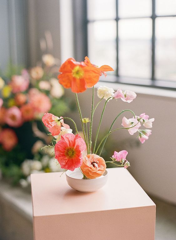 a fantastic wedding centerpiece of a bowl with red, orange and light pink blooms styled as an ikebana is a lovely idea for spring or summer
