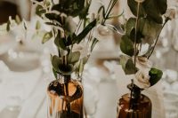 a lovely cluster wedding centerpiece of a stack of books, apothecary bottles with neutral blooms and greenery is a cool idea