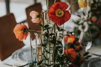 a lovely cluster wedding centerpiece of orange, red and light pink poppies and greenery on the table is amazing for summer