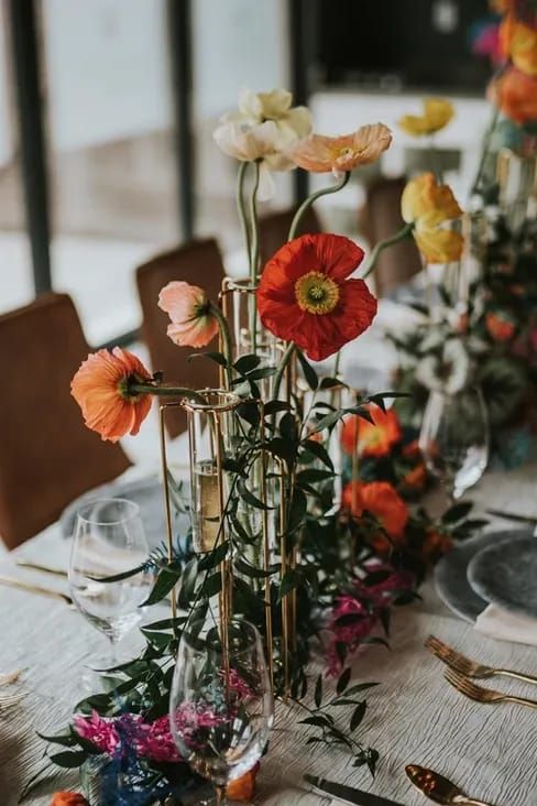 a lovely cluster wedding centerpiece of orange, red and light pink poppies and greenery on the table is amazing for summer