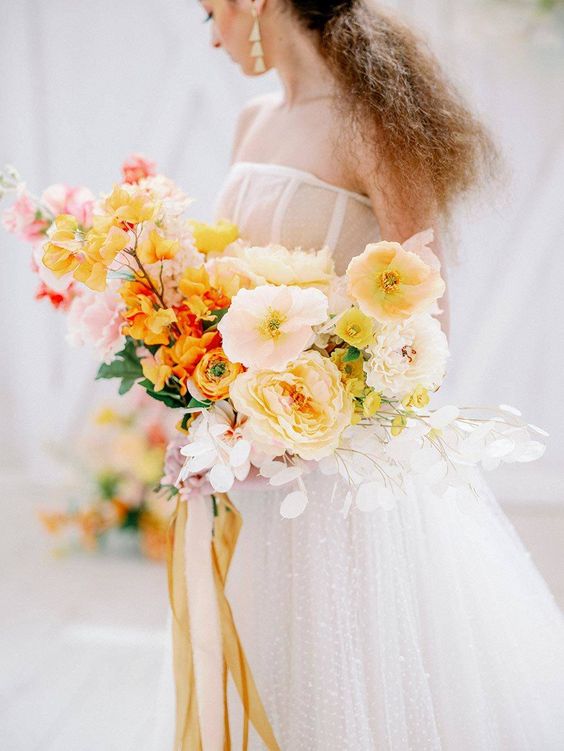 a modern wedding bouquet that includes yellow and light pink poppies, some more yellow and light pink blooms and long ribbons