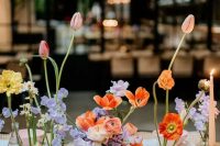 a multi-color cluster wedding centerpiece of orange, red and yellow poppies, orange tulips and ranunculus, lilac flowers