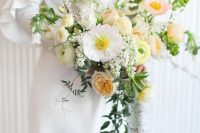 a neutral cascading wedding bouquet of white poppies, neutral and yellow ranunculus, blooming branches and cascading greenery