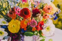 a super bright rustic wedding centerpiece of red, orange, yellow poppes, ranunculus, blue fillers and greenery is amazing