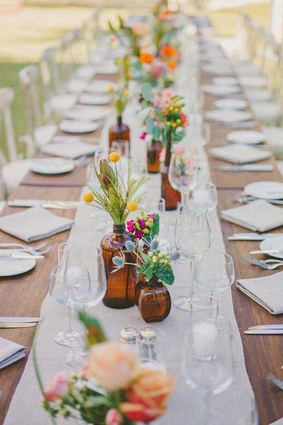apothecary bottles and jars with colorful flowers and greenery and candles for decorating a backyard wedding table
