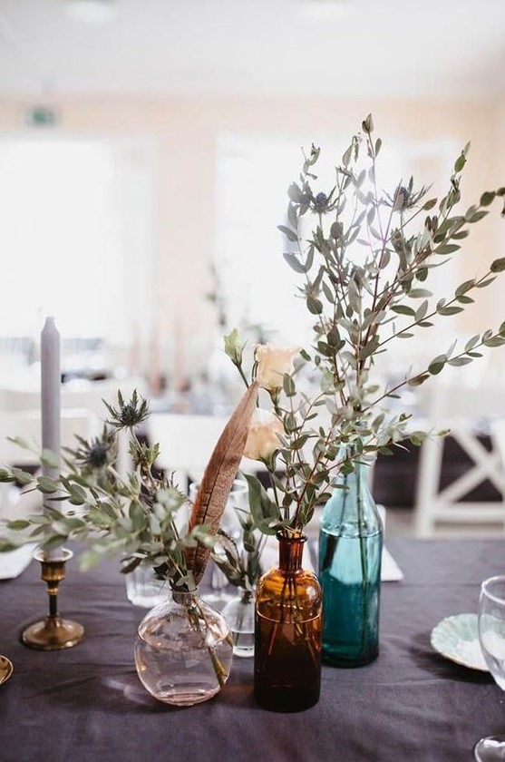 bottles with thistles and eucalyptus, candles and feathers for a boho backyard wedding centerpiece