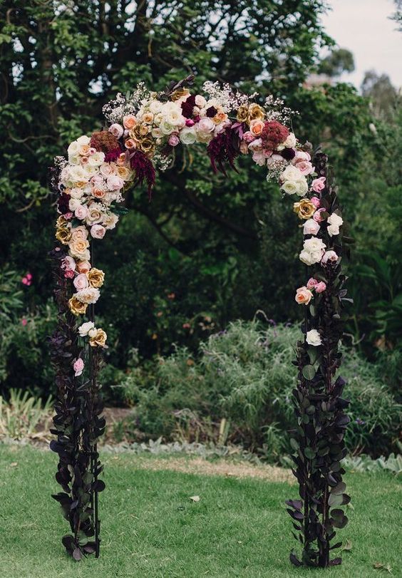 a beautiful moody Halloween wedding arch decorated with dark foliage, with neutral, pastel and dark blooms