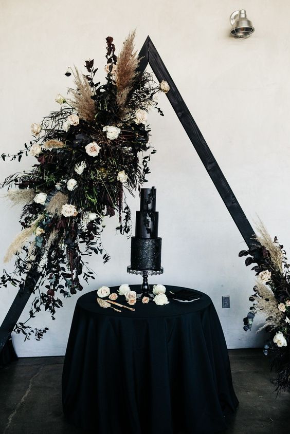 a black triangle wedding arch decorated with neutral and deep purple blooms, pampas grass, greenery and dark foliage is a gorgeous idea for Halloween