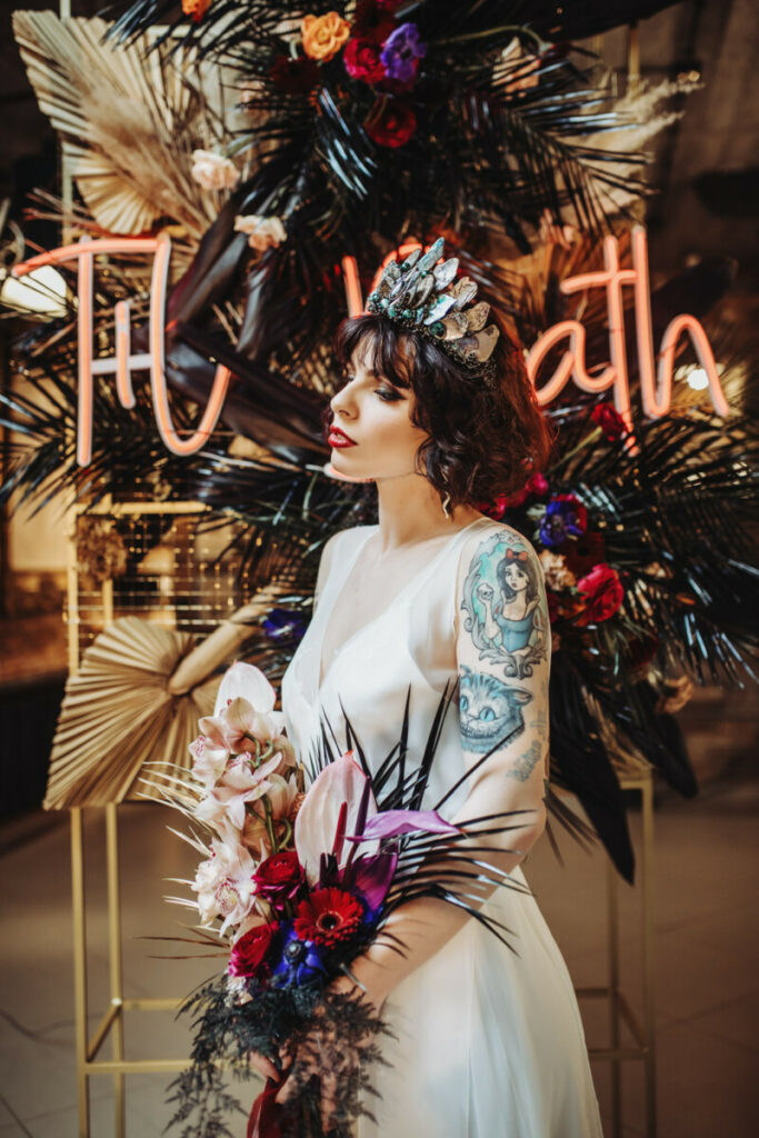a gorgeous romantic rock n roll bridal look with a silk slip wedding dress, bold tattoos shown off and a statement colorful crown and bouquet