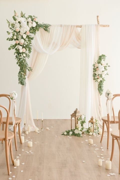 a delicate and chic neutral wedding ceremony space with neutral fabric, blooms and greenery, vintage candle lanterns and petals on the floor