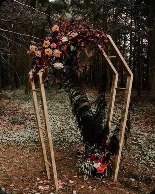a coffin-shaped wedding arch styled with dark foliage, bold and pastel blooms, dark pampas grass and greenery for a Halloween wedding