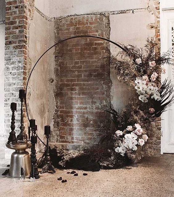a fantastic round wedding arch decorated with neutral and blush blooms, dark leaves and foliage, black candles in candleholders for a Halloween wedding