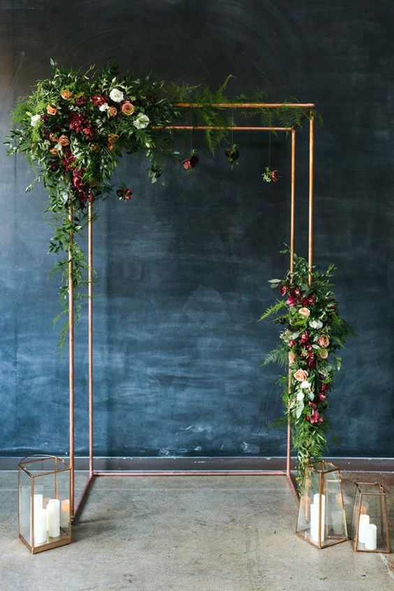 a laconic modern wedding chuppah decorated with greenery, neutral and bold blooms and chic copper candle lanterns is amazing