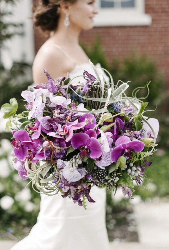 a breathtaking wedding bouquet with purple and neutral orchids, greenery, berries, feathers and air plants is a bold solution