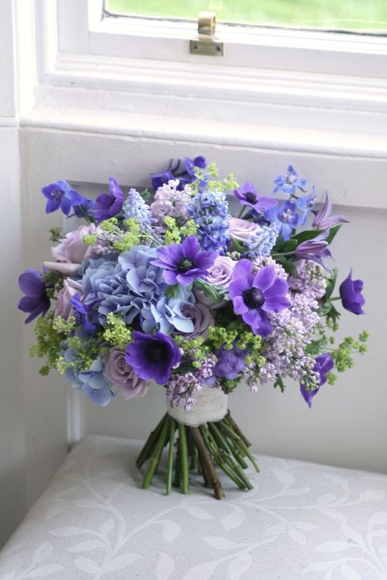 a bright wedding bouquet with purple, violet, blue and pale lilac blooms and greenery is lovely for a bold summer wedding