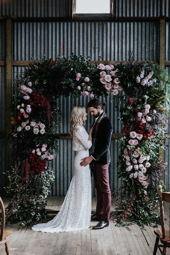 a sophisticated Halloween wedding arch decorated with greenery, light pink and deep red blooms is a chic idea for a wedding