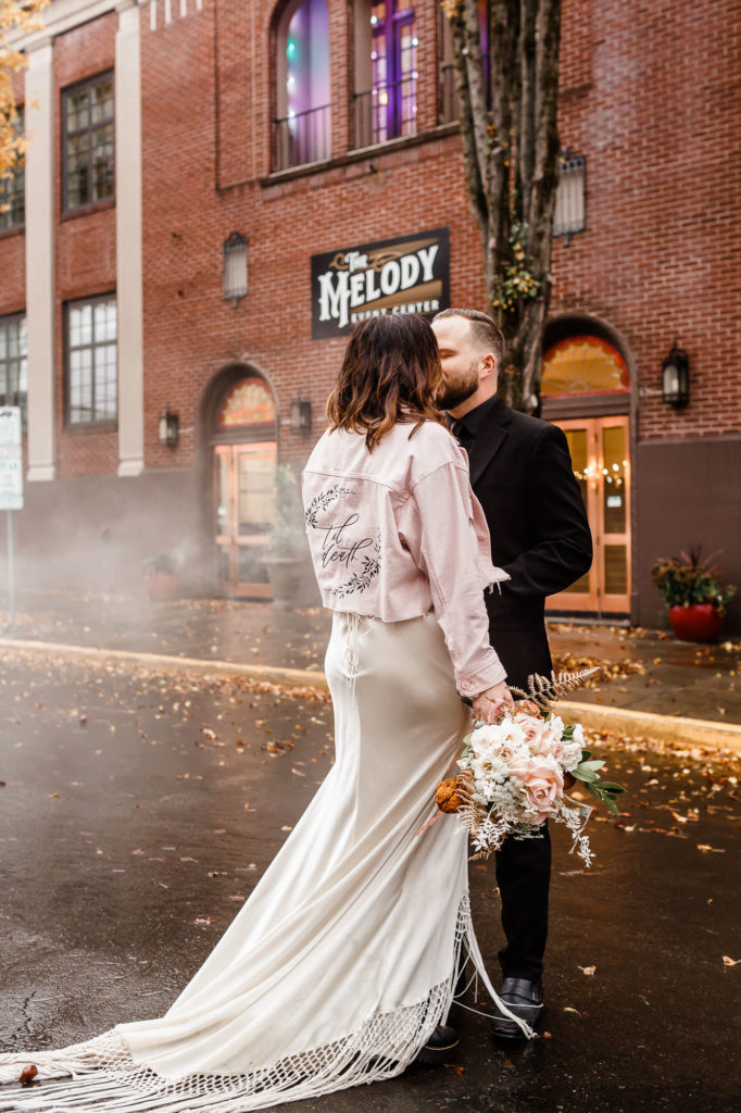 a delicate and romantic rock n roll bridal look with a neutral slip wedding dress with a train and fringe, a pink painted denim jacket and black leather boots