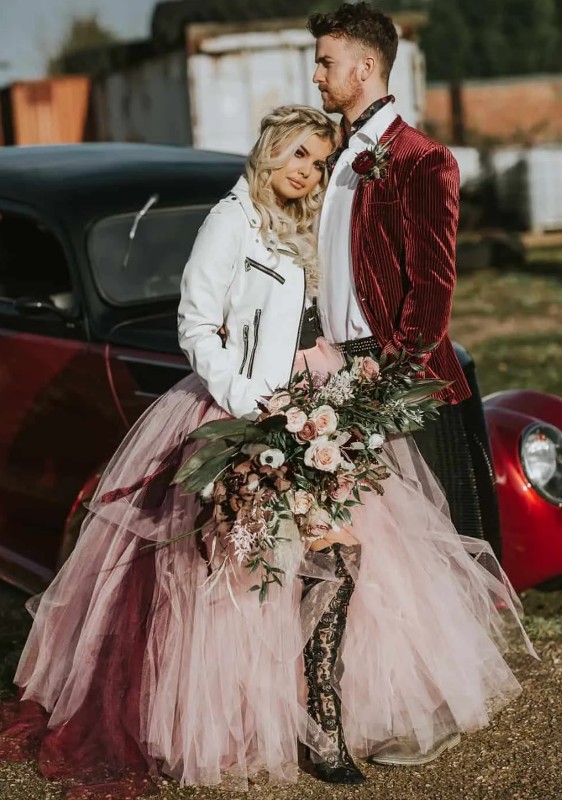 a glam rock bridal look with a corset, a blush tutu skirt with a burgundy train, a white leather jacket and black lace high boots