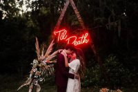 16 a triangle Halloween wedding arch decorated with neutral and pastel blooms and pampas grass and a red neon sign is amazing