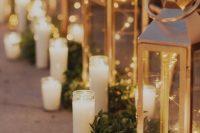 16 a wedding aisle lined up with giant candle lanterns with candles and LED lights, greenery runners and tall and thin candles