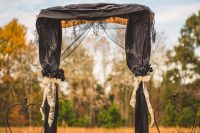 17 a whimsical Halloween wedding arch with black curtains and black blooms and foliage, white ribbon bows, blackened pumpkins on stands