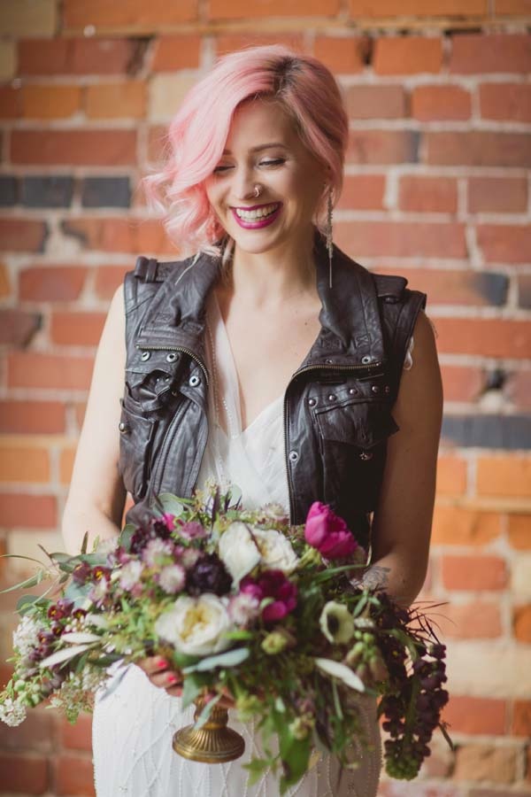a lovely rock n roll bridal look with a romantic embellished wedding dres,s a black leather waistcoat, pink hair, piercings and a hot pink lip