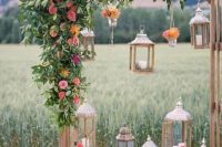 18 a wedding arch decorated with greenery and bold blooms, crates with wooden candle lanterns and some lanterns hanging down
