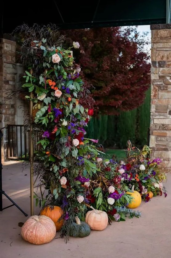 a fantastic wedding backdrop of a floral arrangement with violet, blush, burgundy and orange blooms, lush foliage and greenery and pumpkins