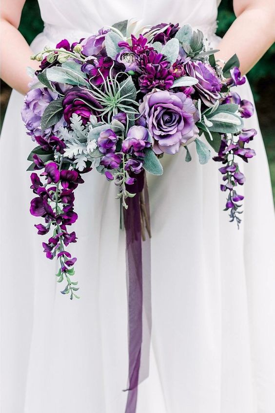 a jaw dropping cascading purple wedding bouquet with purple blooms, air plants, leaves and long ribbon for a fall bride
