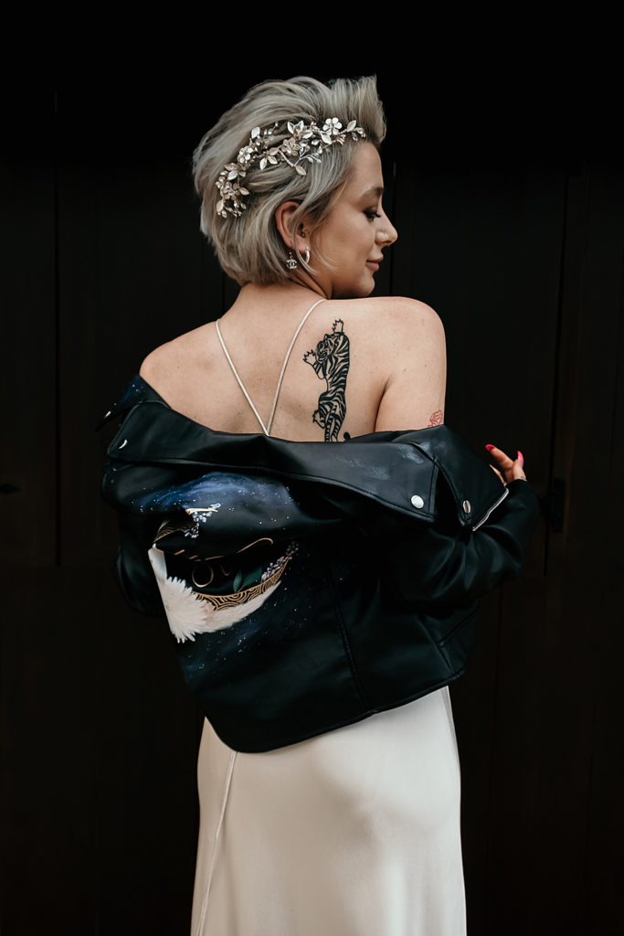a modern rock n roll bridal look with a silk slip wedding dress, a painted black leather jacket, a statement rhinestone headpiece
