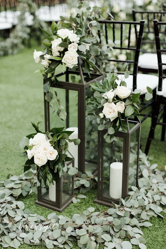 a wedding ceremony space done with greenery, black candle lanterns and white blooms on top is a lovely idea for a wedding