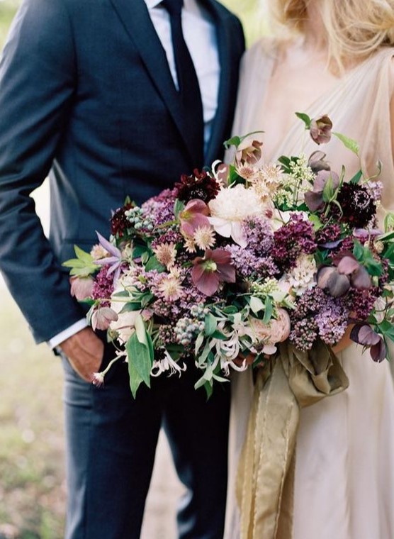 a moody wedding bouquet with purple, pink and neutral blooms, greenery and some berries for a fall or summer wedding