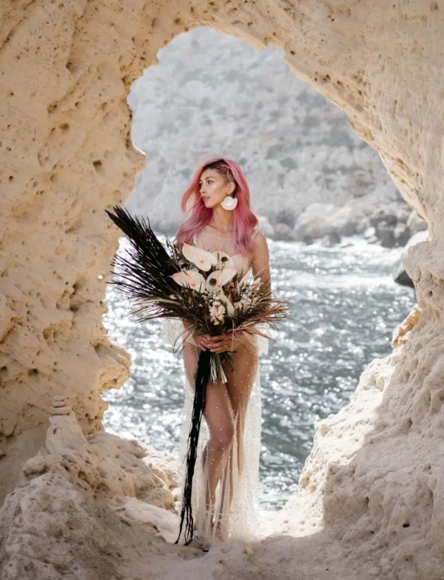 a unique bridal look with a creamy bodysuit, a neutral sheer pearl wedding dress, statement earrings and lace up shoes, pink hair