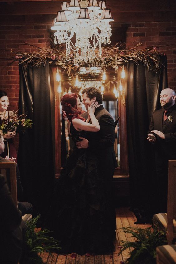 a Halloween wedding backdrop with black curtains, twigs and branches and dark blooms is a great idea to realize