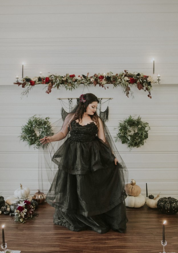 a modern Halloween wedding altar with dark and deep red blooms and greenery, tall and thin candles, greenery wreaths and black macrame, stacked pumpkins