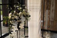 29 a modern wedding sign on a black frame, with sleek modern candle lanterns, white blooms with greenery on a tall stand is super chic