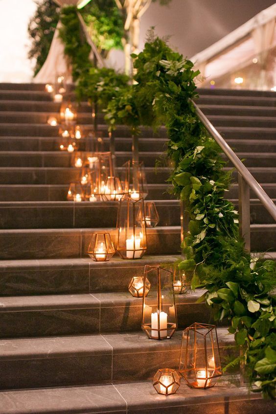 a wedding staircase decorated with a lush greenery runner and faceted copper candle lanterns on the steps