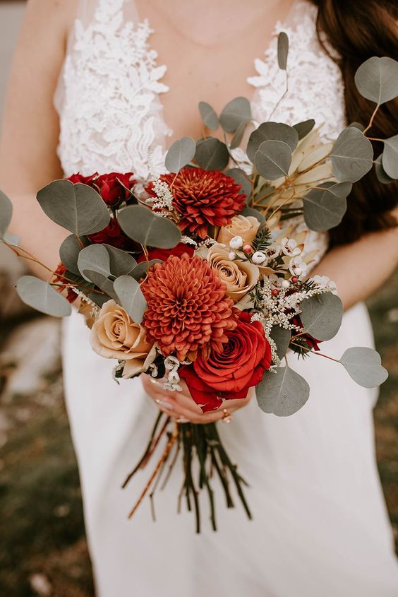a beautiful fall wedding bouquet with coffee roses, burnt orange dahlias and roses, greenery, berries and waxflowers is cool