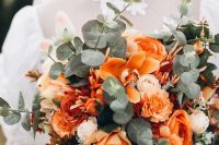 a beautiful fall wedding bouquet with orange roses, orchids, blush blooms, eucalyptus and dark foliage is a chic idea