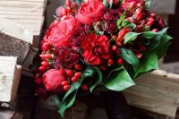 a bold and catchy wedding bouquet of burgundy roses and red peonies, greenery and red berries is a lovely idea for a bold bridal look