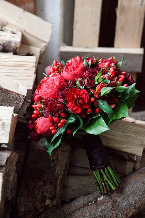 a bold and catchy wedding bouquet of burgundy roses and red peonies, greenery and red berries is a lovely idea for a bold bridal look