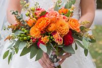 a bold and chic fall wedding bouquet of orange dahlias, ranunculus, roses, burgundy dahlias, berries and greenery