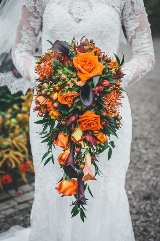 a bold cascading fall wedding bouquet with orange roses and pincushion proteas, dark callas, berries and greenery is a fantastic idea