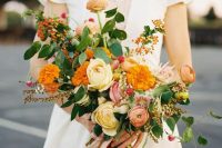 a bold fall wedding bouquet of light yellow, orange and coral blooms, greenery, berries and long ribbon is wow