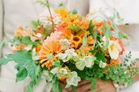a bright and cool orange wedding bouquet of light pink, red and orange blooms, textural greenery of various kinds