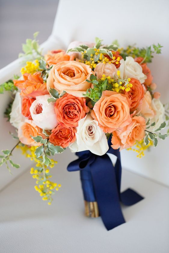 a bright and cool orange wedding bouquet of roses, blush and white peony roses, greenery, mimosa and navy ribbon