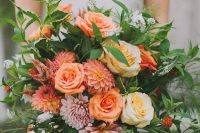 a bright fall wedding bouquet with orange dahlias, roses, yellow roses and pink dahlias, greenery and some berries
