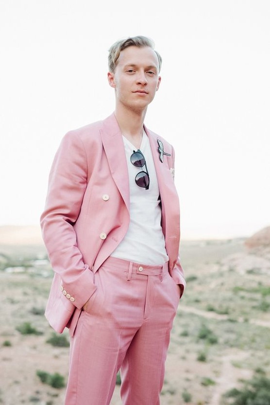 a bright pink groom's suit with a white t-shirt, sunglasses and a unique boutonniere for an offbeat wedding